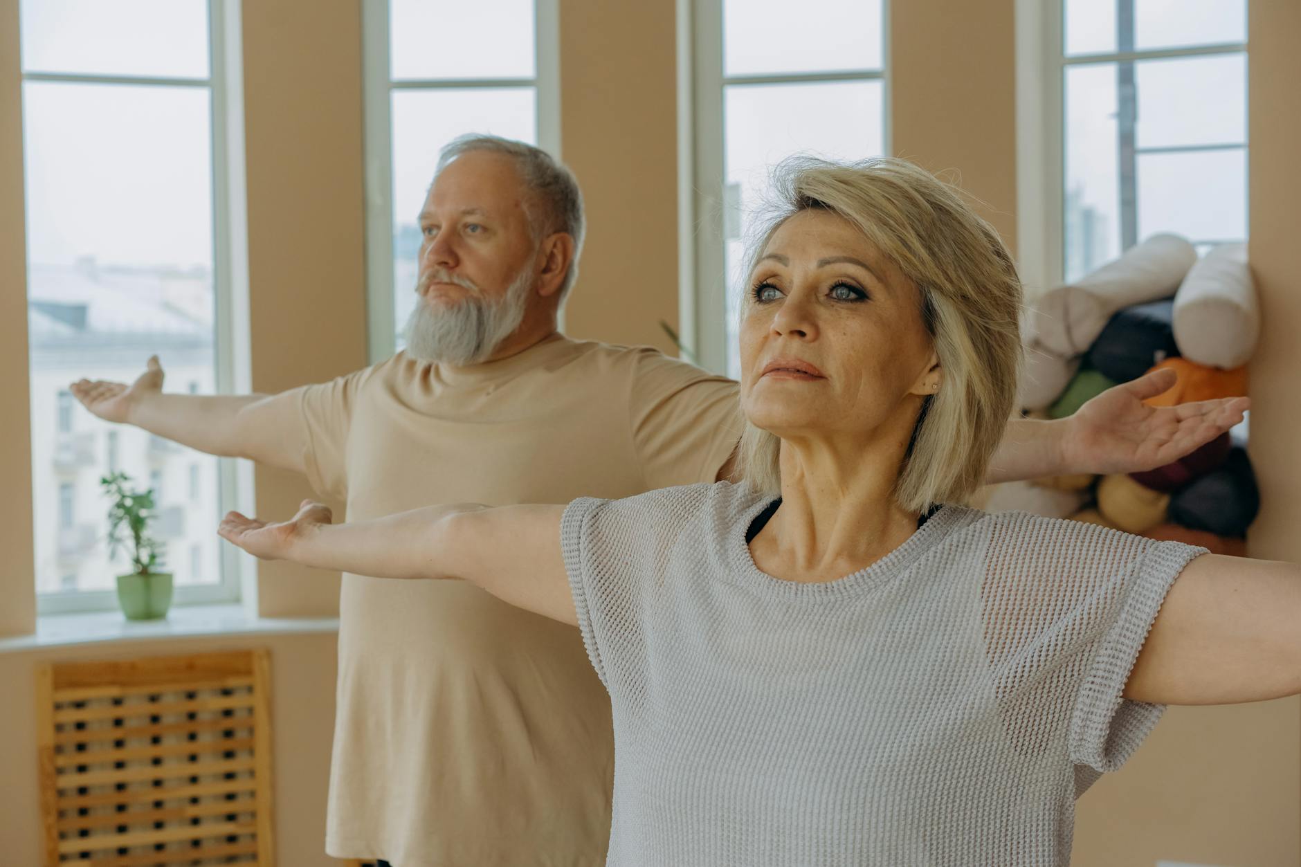 Ćwiczenia oddechowe po COVID-19: praktyczny przewodnik fizjoterapeuty dla dorosłych i seniorów Starsze małżeństwo ćwiczy jogę z wyciągniętymi ramionami w jasnym pokoju